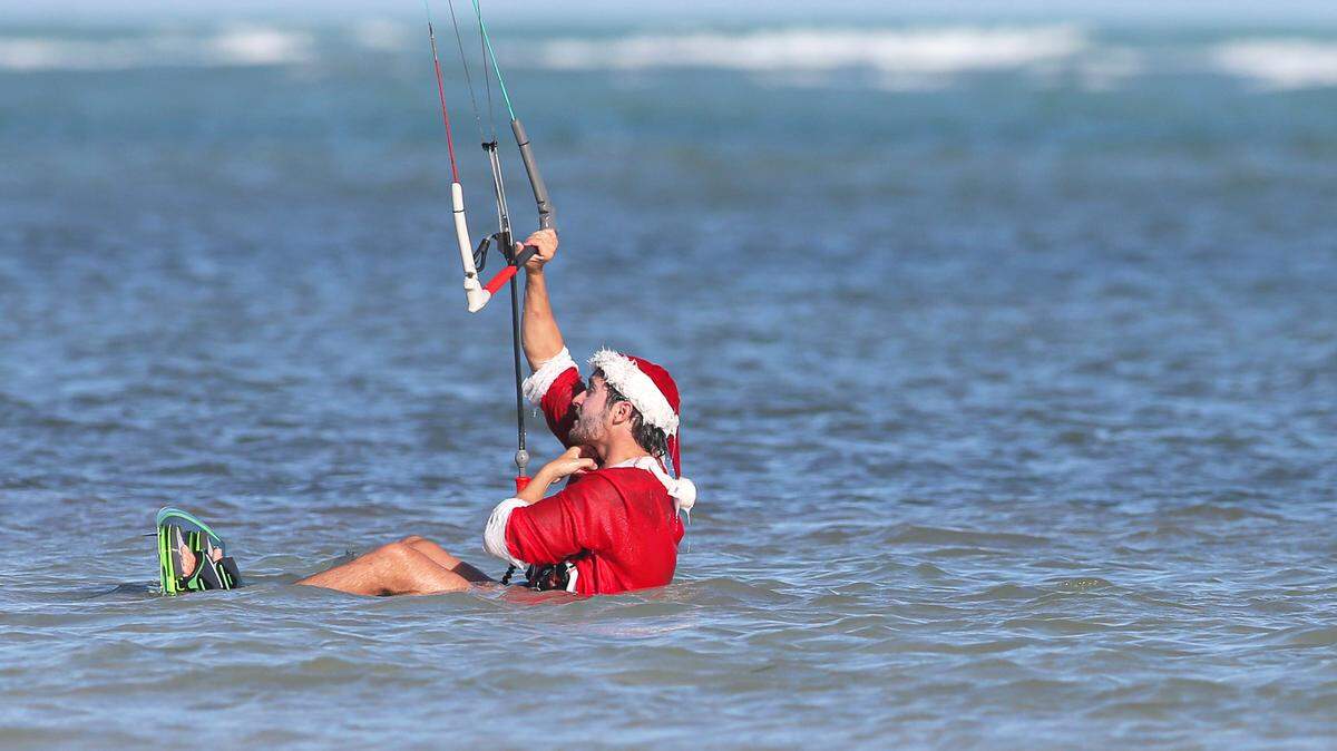 In this file photo from Dec. 31, 2020, Mat Nittmann wears a Santa Claus costume while kiteboarding at Crandon Park Beach in Key Biscayne, Florida. The weather forecast for Christmas Week 2025 calls for comfy temperatures so don’t rule out Santa swims.