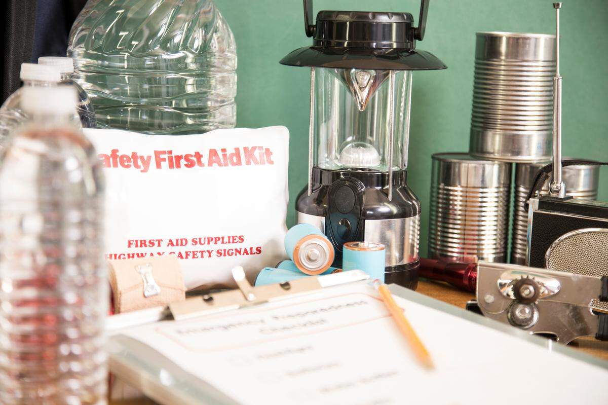 A pile of emergency preparation, natural disaster supplies including: checklist, flashlight, first aid kit, lantern, water bottles, canned goods, can opener, radio, backpack, batteries. When it’s hurricane season it’s best to be prepared.