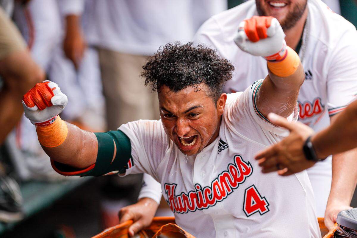Miami Hurricanes catcher Maxwell Romero Jr. (4) celebrates by riding the laundry cart inside the dugout as his teammates splash him with water after hitting a home run in the fourth inning against Notre Dame at Alex Rodriguez Park at Mark Light Field in Coral Gables, Florida on Saturday, May 21, 2022.