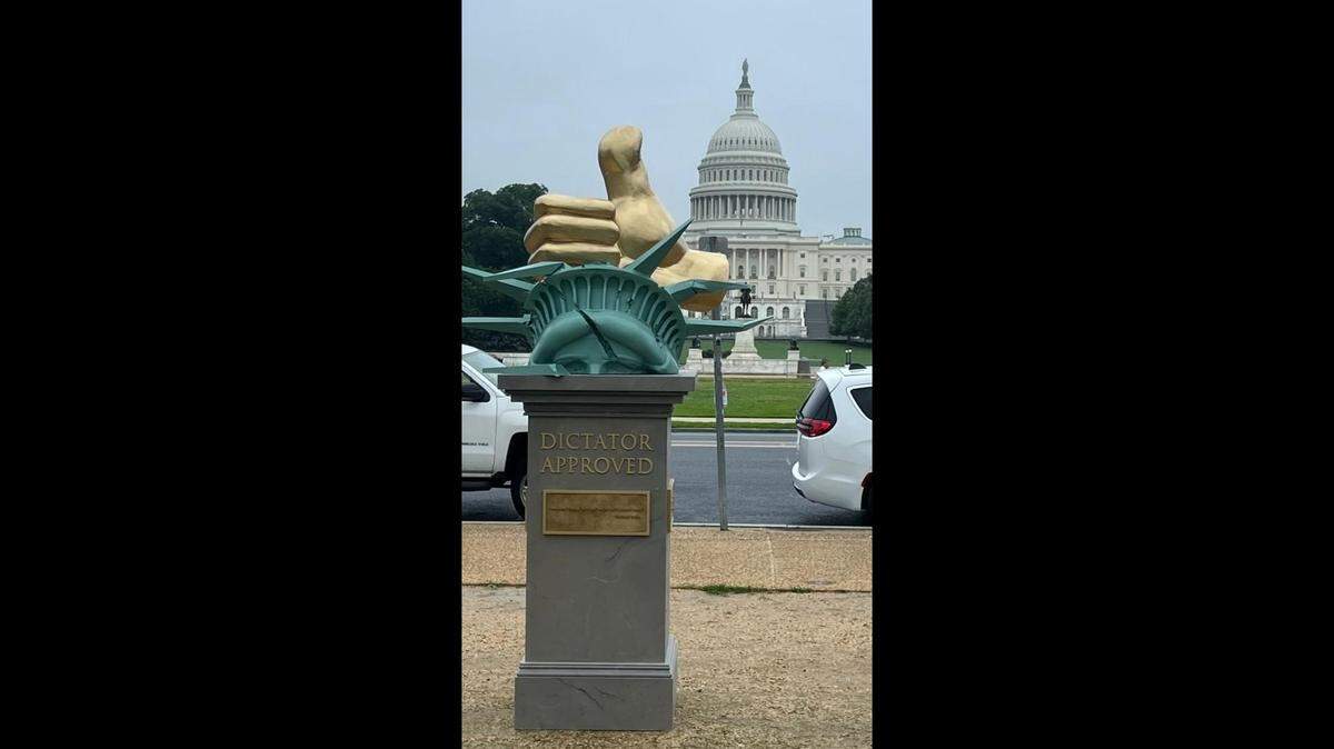 A sculpture portraying a large “thumbs up” gesture squashing the Statue of Liberty’s head appeared on the National Mall and includes text referencing President Donald Trump.