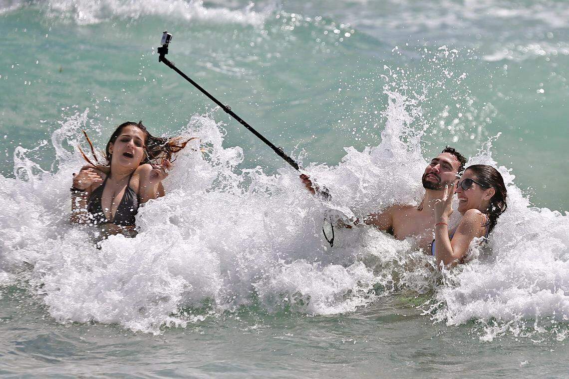 FIU spring breakers Miguel Irias, 22, holds a selfie stick as he videos his friends in the surf, Valerie Rincon, 22, left and Jennifer Perez, 22, at right, on South Beach on Tuesday, March 10, 2015.