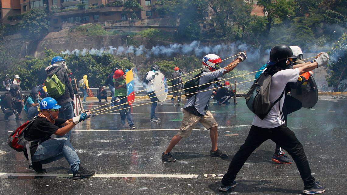In this May 10, 2017, file photo, anti-government protesters work together to aim a giant slingshot holding a glass bottle filled with feces, at security forces blocking their march from reaching the Supreme Court in Caracas, Venezuela. Protesters write messages like "For the political prisoners!" and "Sent with love" on the containers.