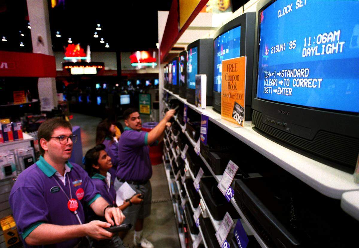 Employees at an Incredible Universe store program the VCRs.