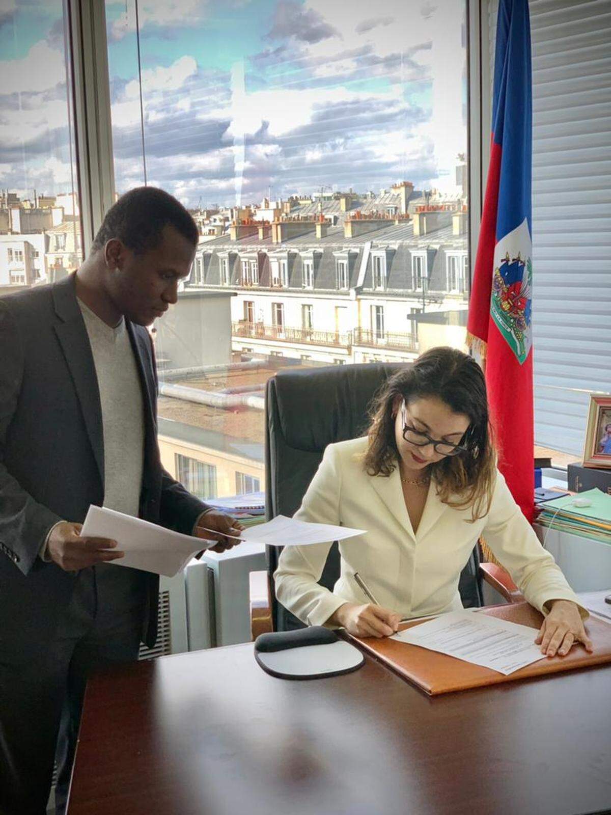 Haiti’s UNESCO Ambassador Dominique Dupuy (seated) signs the candidacy of soup joumou for the Intangible Cultural Heritage of Humanity list in Paris, France, March 25, 2021. Dupuy is joined by Ricarson Dorcé, an expert on cultural heritage for the Haiti delegation.