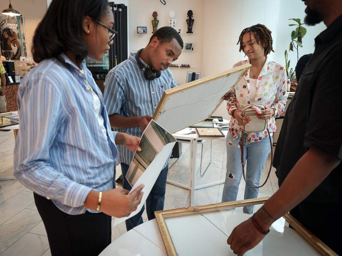 Curators Cade Hardy, 16, left, Alford Archer, 15, and Shayna Lewertow, 17, begin framing the artwork for installation with help from Nyya Toussaint, right. Four high school students installed photos inside the First Church Miami coffee shop for the exhibition Sparrow, featuring the photography of local photographers navigating homelessness under the artistic direction of Miami-based artist Christopher Mitchell on Sunday, November 30, 2025.