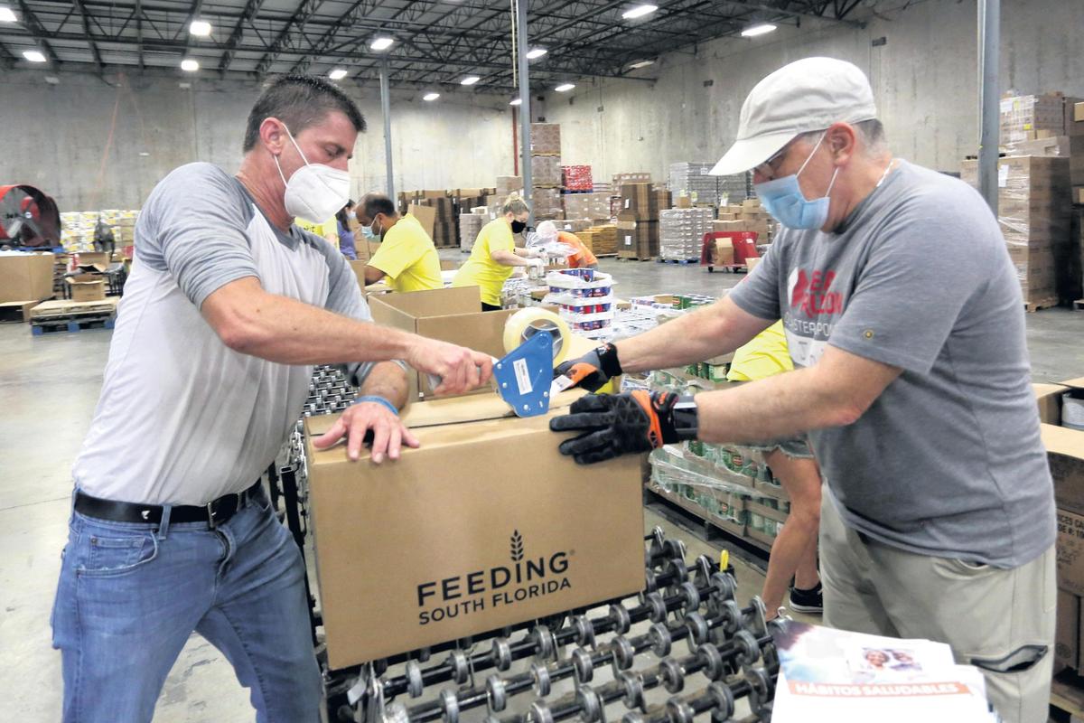Volunteer workers at Feeding South Florida Kenny Albury, 48, left, and John Young, 66, prepare food packages for distribution containing dairy, produce and protein to support the area’s most vulnerable populations during the pandemic at the food distribution warehouse on 2501 SW 32nd Terrace in Pembroke Park.