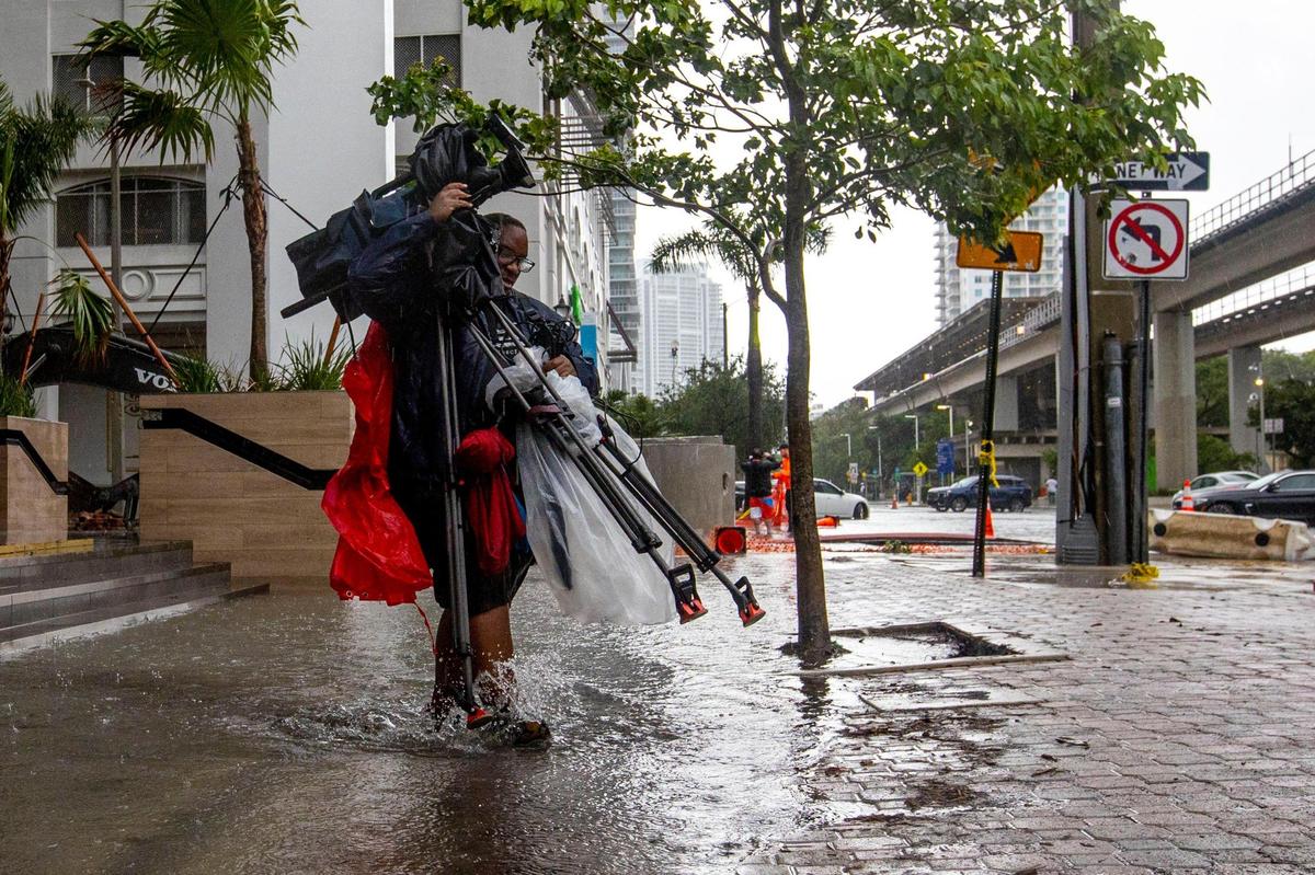 A TV cameraman lifts his gear as he walks through a flooded side walk due to rain near Southwest First Avenue and Southwest Ninth Street in the Brickell neighborhood of Miami, Florida, on Saturday, June 4, 2022.