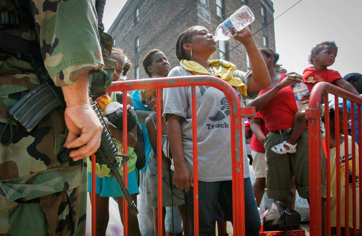 As National Guard look on from left, a woman guzzles water while she waits for a bus to carry her to an unknown destination on Friday September 3, 2005, six days after hurricane Katrina ripped through the Gulf Coast leaving thousands homeless in New Orleans, a mass evacuation took place from streets near the Ernest N. Morial Convention center that housed thousands awaiting evacuation.