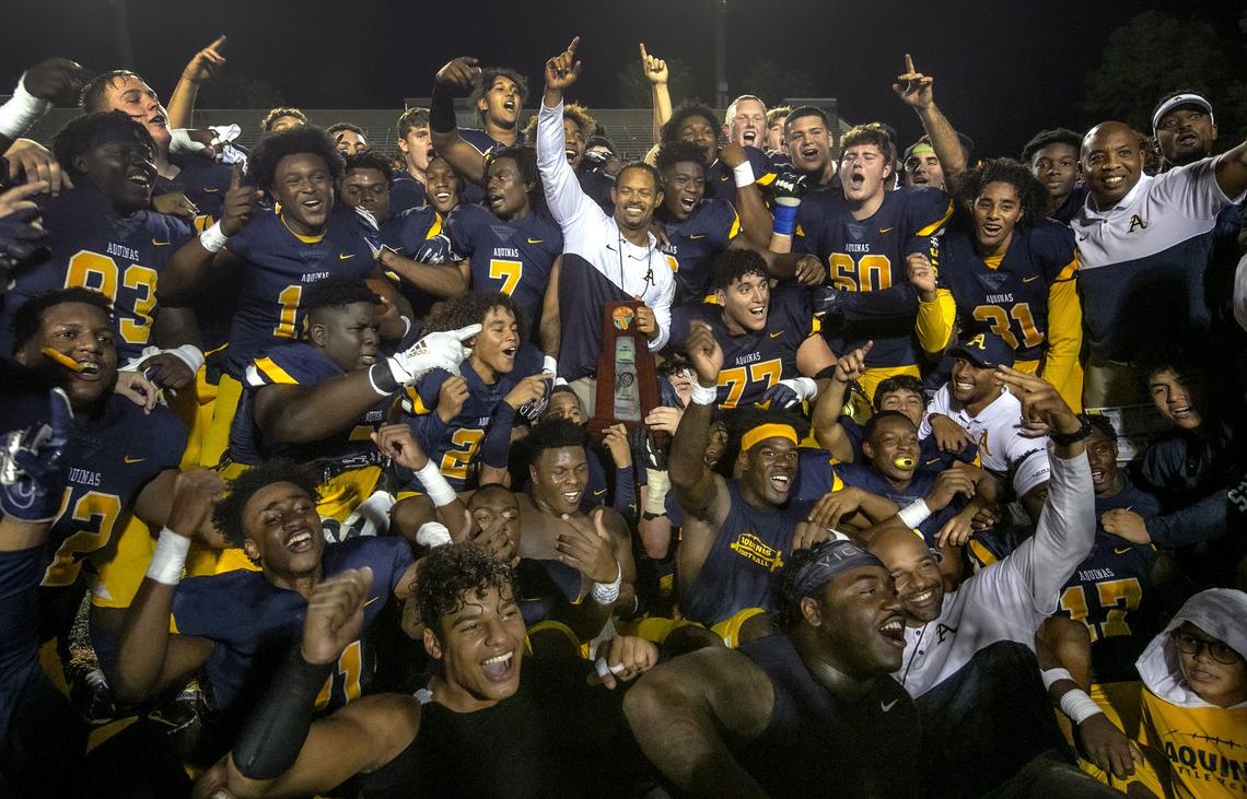 St. Thomas Aquinas head coach Roger Harriott holds the championship trophy as the team celebrates after St. Thomas Aquinas Raiders defeats Edgewater Eagles 23-28 for the Class 7A FHSAA State Championship at Daytona Stadium in Daytona Beach on Saturday, December 14, 2019.