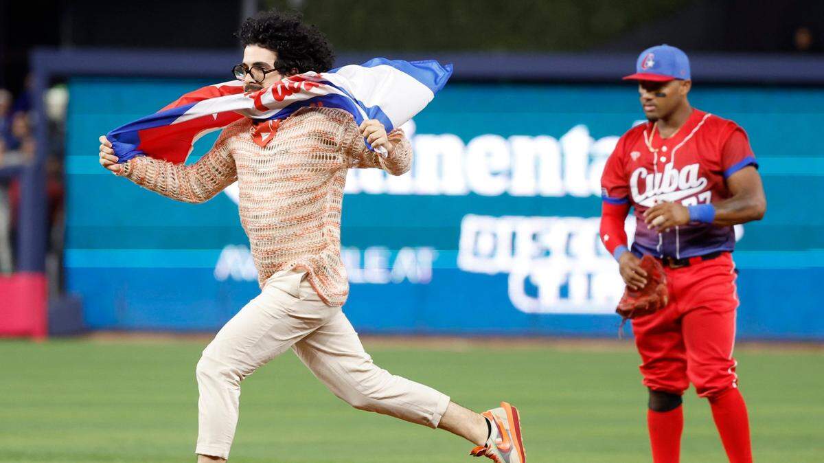 Cuban journalist Carlos Manuel Alvarez carrying a Cuban flag with the words Patria y Vida runs on the field as Cuba infielder Andy Ibáñez (77) looks on during the game between the United States and Cuba at the World Baseball Classic semifinal at loanDepot Park in Miami, Fla. on Sunday, March 19, 2023.