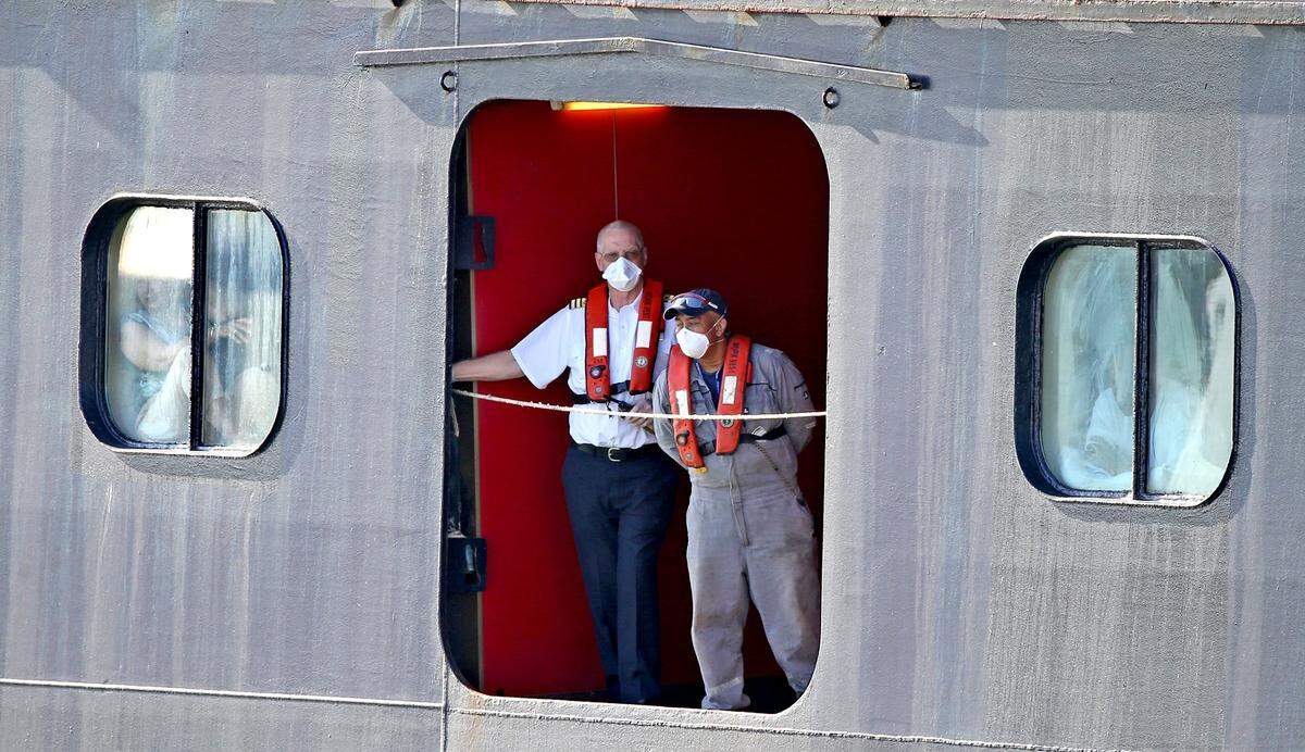 A passenger sits in the window as crew watch as the Rotterdam docks at Port Everglades in Fort Lauderdale, Florida, April 2, 2020. Zaandam cruise ship with COVID-19 on board also docked after 12 days at sea.