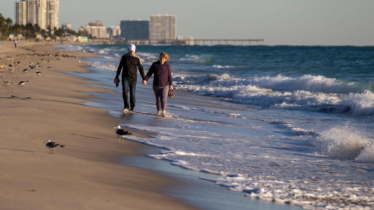 Jason Rayburn and Natalie Suiter walk near the shoreline as temperatures dip into the mid-40s on Saturday, Jan. 14, 2023, in Hollywood, Florida.