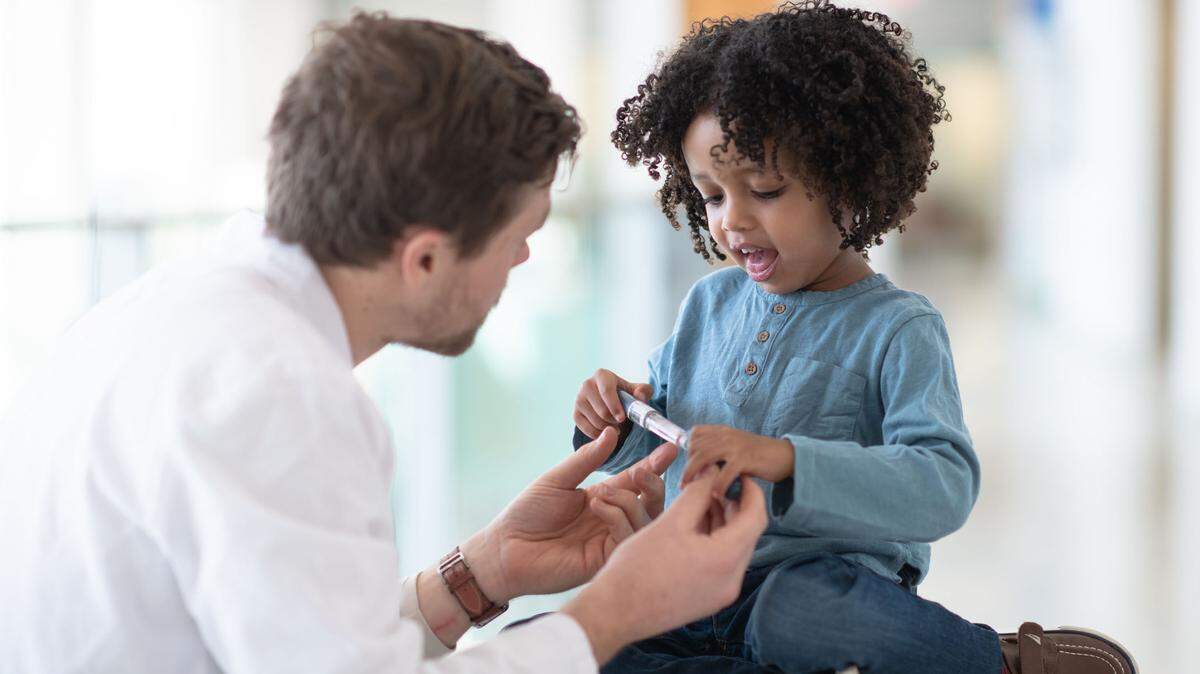 A boy of 4 or 5 years looks down at the diabetes pen his doctor his showing him with intrigue.