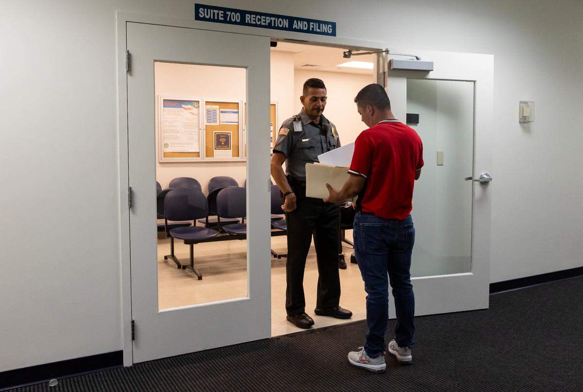 Un oficial de seguridad escucha las preguntas de una persona en el Tribunal de Inmigración en el centro de Miami.