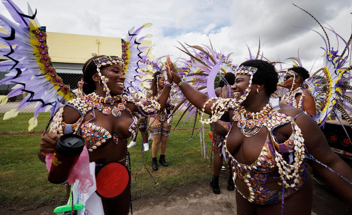 Paula Maynard, left, high fives, Sharleen Vasquez while dancing before their band called “Party Room Squad” lines up for the Parade of Bands at Miami Carnival on Sunday, Oct. 13, 2024, at Miami-Dade County Fair Expo.