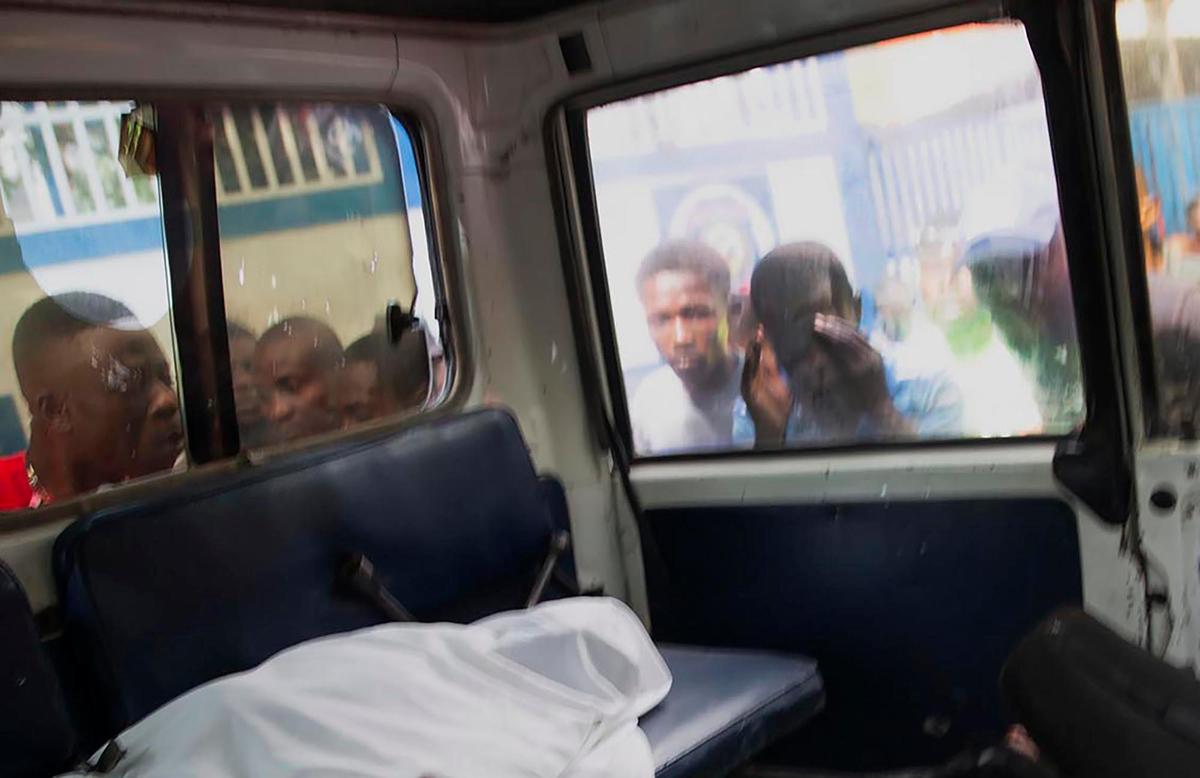 Unas personas miran por la ventanilla de un vehículo policial que lleva los cuerpos de dos personas muertas en un tiroteo con la policía en Puerto Príncipe, Haití, el jueves 8 de julio de 2021. Según el jefe de policía Leon Charles, los dos muertos son sospechosos del asesinato del presidente haitiano Jovenel Moïse.
