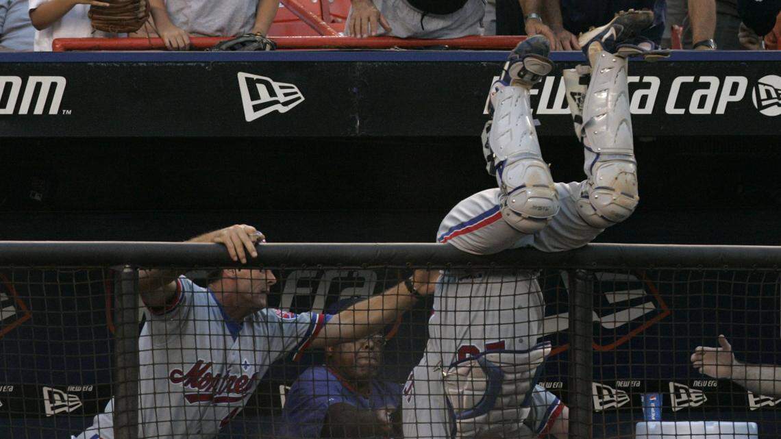 Montreal Expos catcher Brian Schneider, right, goes over the rail after catching a foul ball hit by New York Mets’ David Wright in his first major-league at-bat as Randy St. Claire reaches in to grab him on July 21, 2004, in New York.