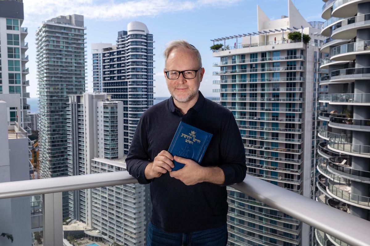 Daniel Gammerman stands on his apartment balcony overlooking the Brickell neighborhood as he holds his Jewish prayer book. Gammerman has struggled to find an Orthodox synagogue in his area that will accept him as a gay man.