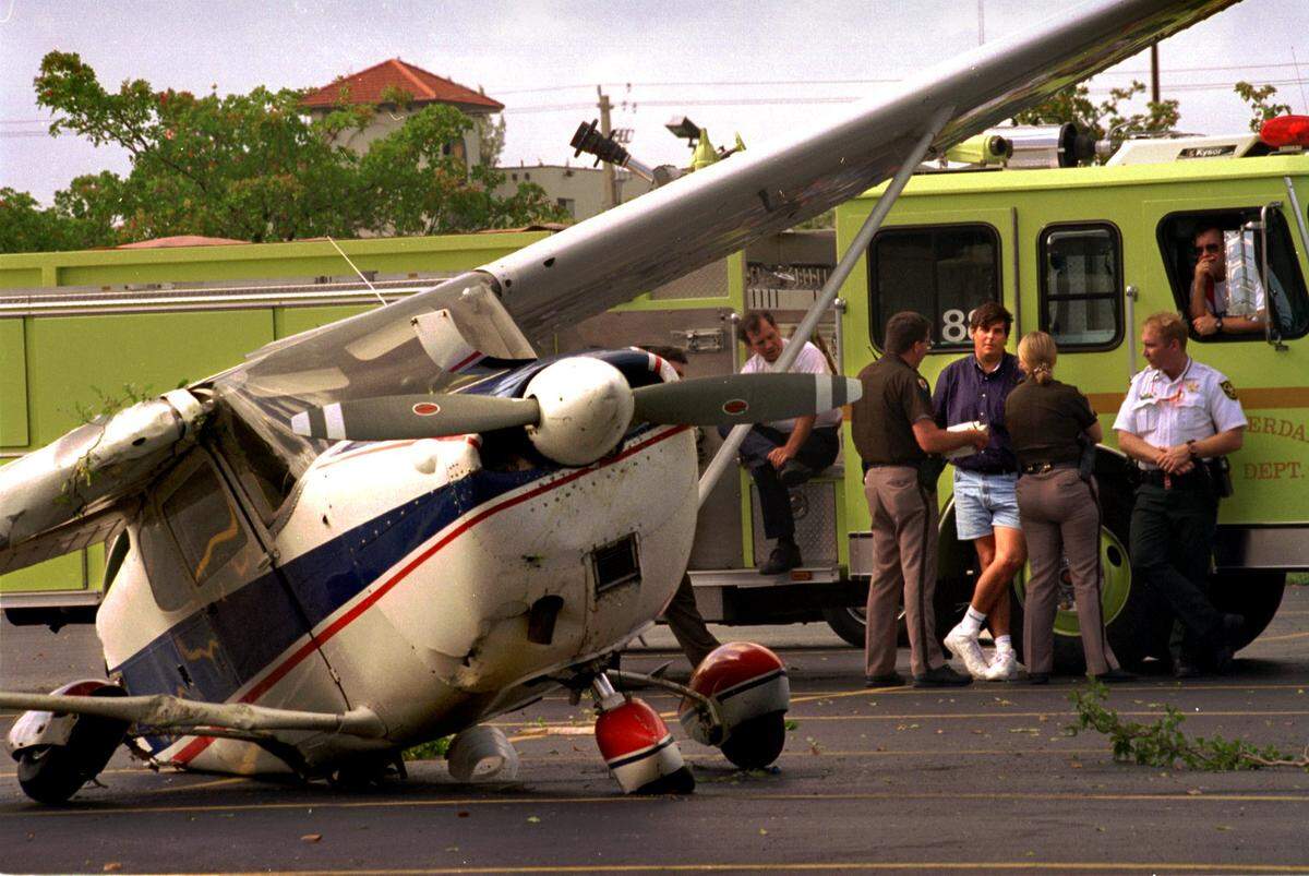 Fort Launderdale officers and Broward deputies talk with the pilot (in the shorts) of a small plane that made a crash-landing in the parking lot of the Levitz furniture store at Powerline Road and 62nd. Street on April 13, 1995.