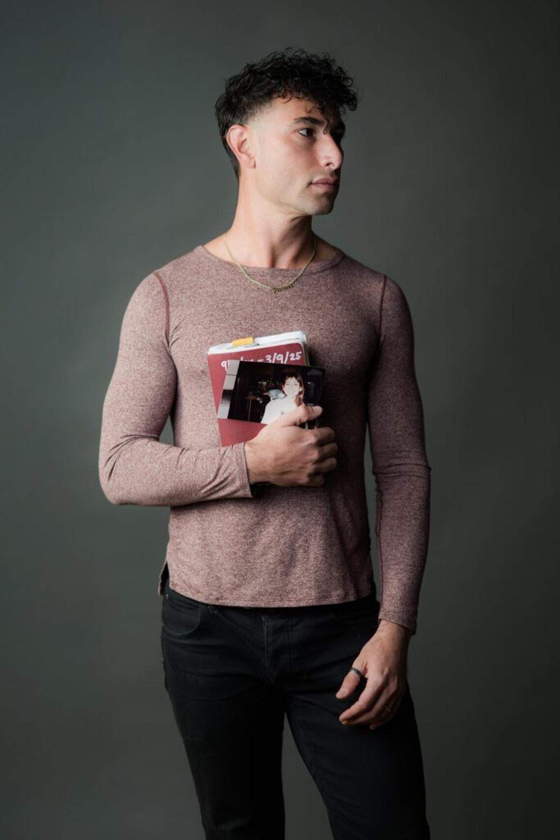 Portrait of Pioneer Winter, holding a notebook and a photo of his mom with her African grey, for “In the Belly of the Bird/Godmother.”
