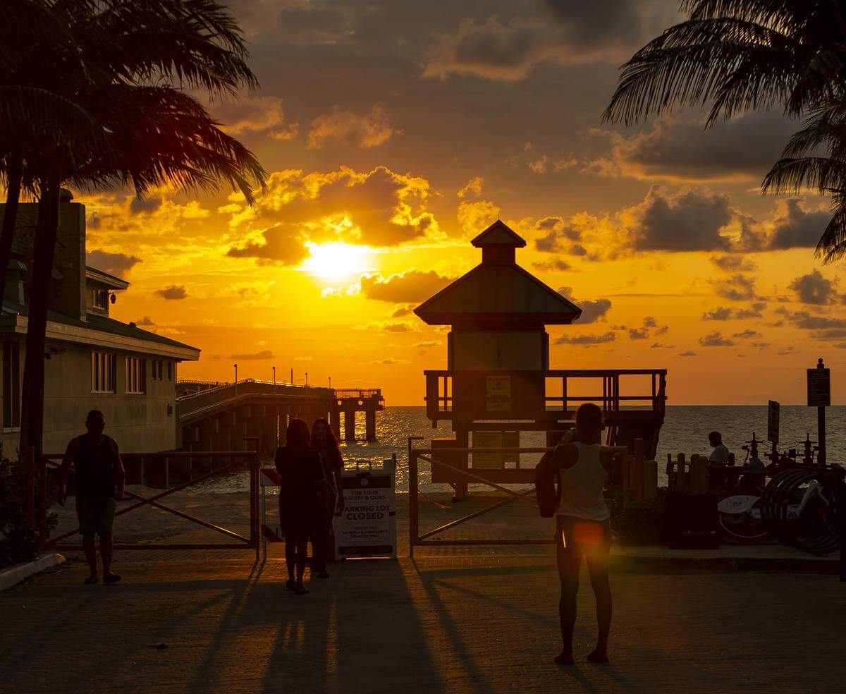Un grupo de personas toma fotos del amanecer en el muelle de Sunny Isles mientras la pandemia del coronavirus continúa, el domingo 5 de abril de 2020, en Sunny Isles Beach.
