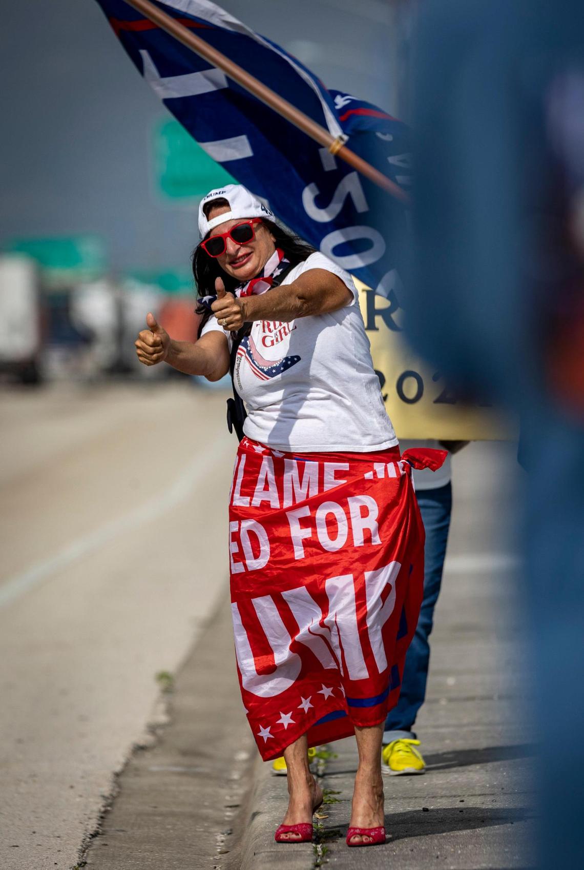 A Donald Trump supporter gives the thumbs up to motorists passing by as she and other people waving flags and signs wait for the former president’s motorcade to pass them on their way to the airport in West Palm Beach, Florida, on April 3, 2023.