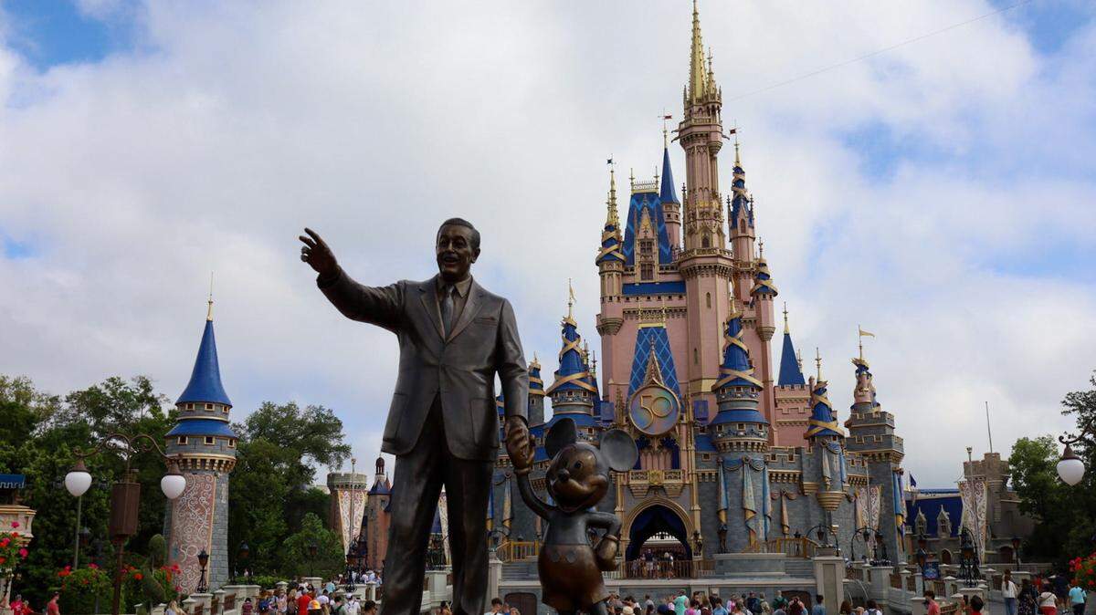 Celebrating the park’s 50th Anniversary, visitors to Disney’s Magic Kingdom pass a statue of Walt Disney holding hands with Mickey Mouse. Disney World Magic Kingdom Walt Disney Statue