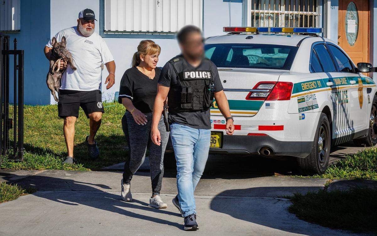 A man holding a dog leaves a house at 11901 SW 185th Terrace Saturday, Jan. 27, 2024, that Miami-Dade County police say was being used as an unlicensed vetinary clinic.