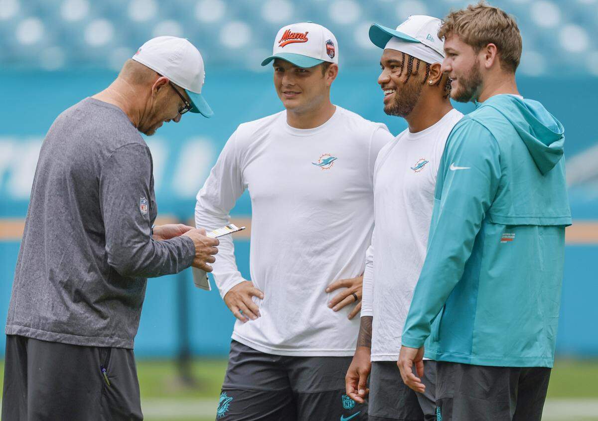 Miami Dolphins quarterbacks Zach Wilson (0), Miami Dolphins quarterback Tua Tagovailoa (1) and Quinn Ewers (14), left to right, huddle with quarterbacks and pass game coordinator Derrell Bevell during pre-game drills before an NFL football game against the Jacksonville Jaguars at Hard Rock Stadium in Miami Gardens, Florida, on Saturday, August 23, 2025.
