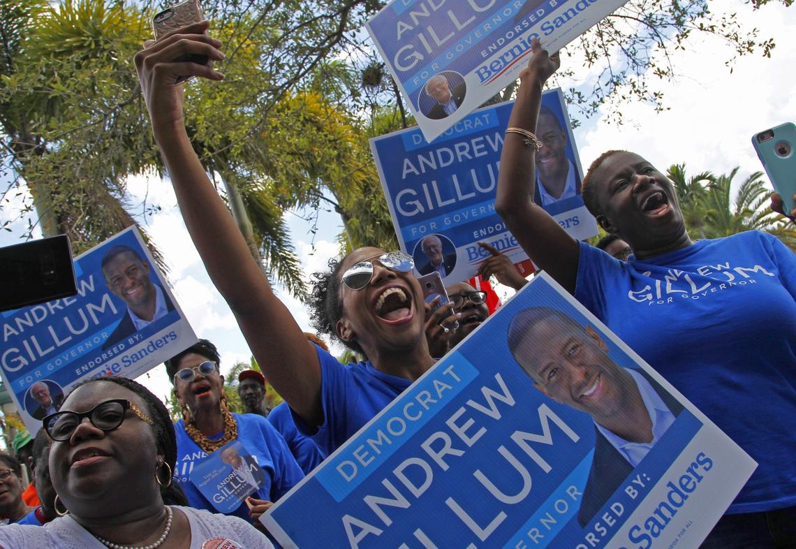 Andrew Gillum supporters Damara Holness, center, and Herdyne Mercier, right, lift their campaign signs along with others as arrival of gubernatorial candidate Andrew Gillum as he took the stage at Reverend Samuel Delevoe Memorial Park during a “Souls to the Polls” event to encourage voter participation and early voting on Sunday, August 26, 2018 in Fort Lauderdale, Florida.