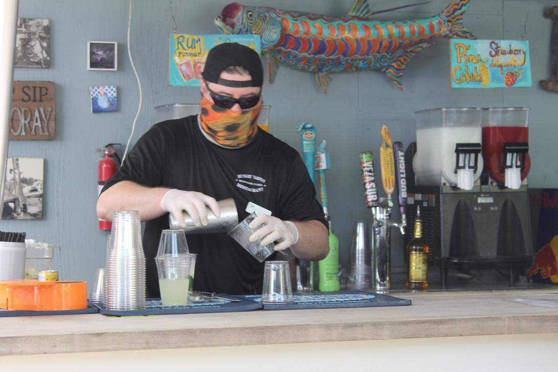 A masked bartender mixes a drink at the Hungry Tarpon Restaurant at Robbie’s Marina Monday, June 1, 2020.