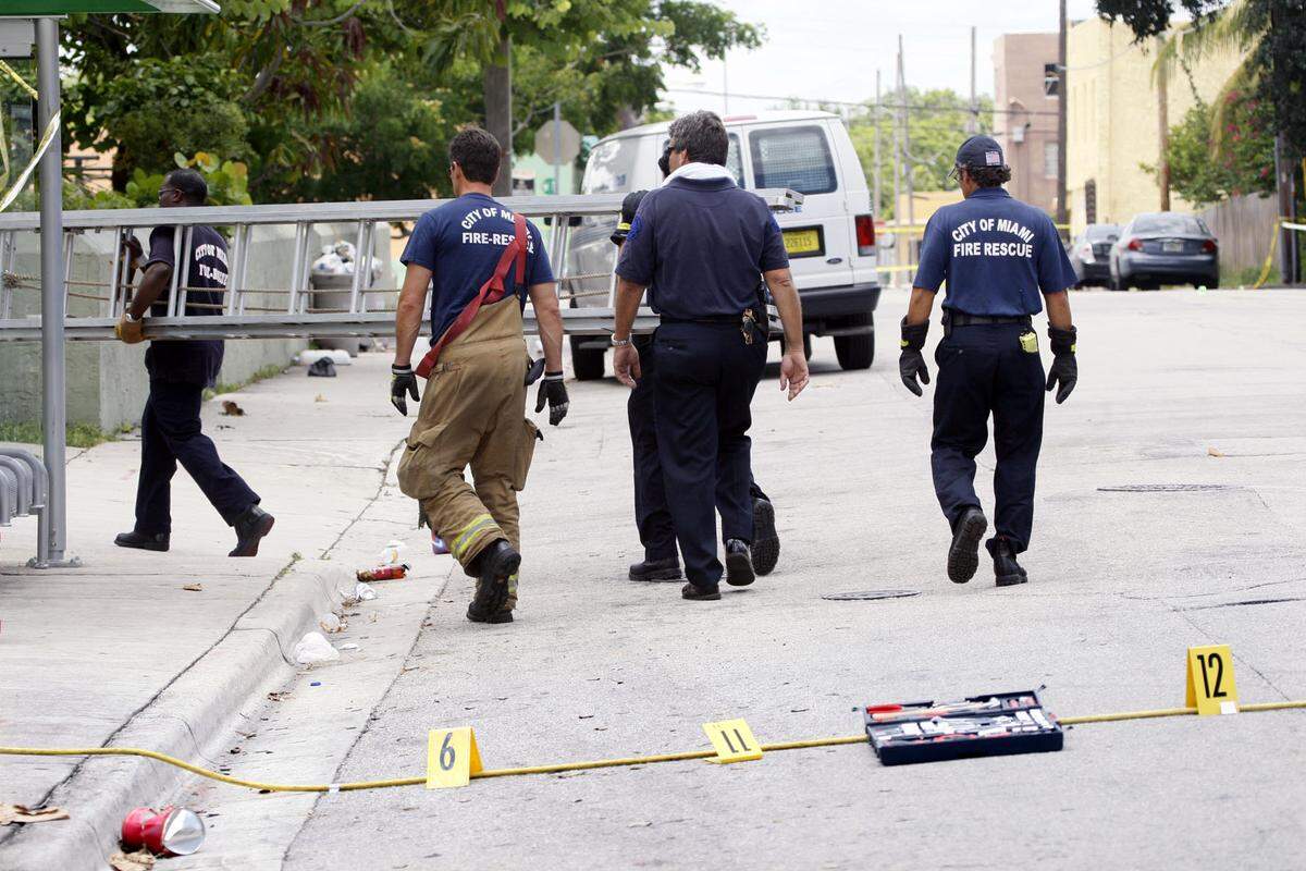 City of Miami Fire Rescue workers on Monday afternoon carry a ladder past markers showing evidence of a shooting at 12:45 a.m. Monday. The employees carried the ladder to the Overtown home where gunfire erupted, during a birthday party that began Sunday night. Twelve people were shot. Miami Police are searching for three shooters. Photo by Marsha Halper / Miami Herald Staff