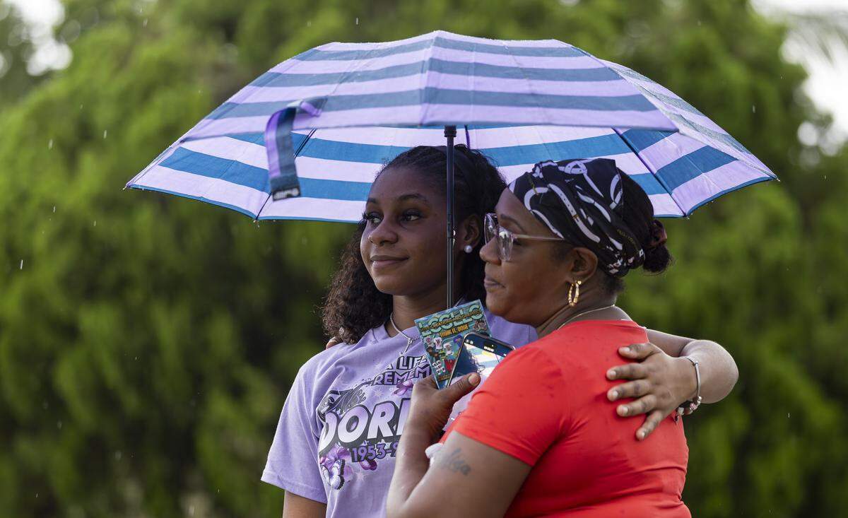Janiah Stephens, left, and her mother, Wylisa Haskins, watch as people visit a makeshift memorial at the site where Doreen Richards Broadbelt was fatally attacked. A vigil was held at Broadbelt's home on Tuesday, Sept. 9, 2025, in Miami Gardens, Fla. Broadbelt, 71, was walking to her job at Walmart when a dog attacked and fatally mauled her near her home on Labor Day, police said.