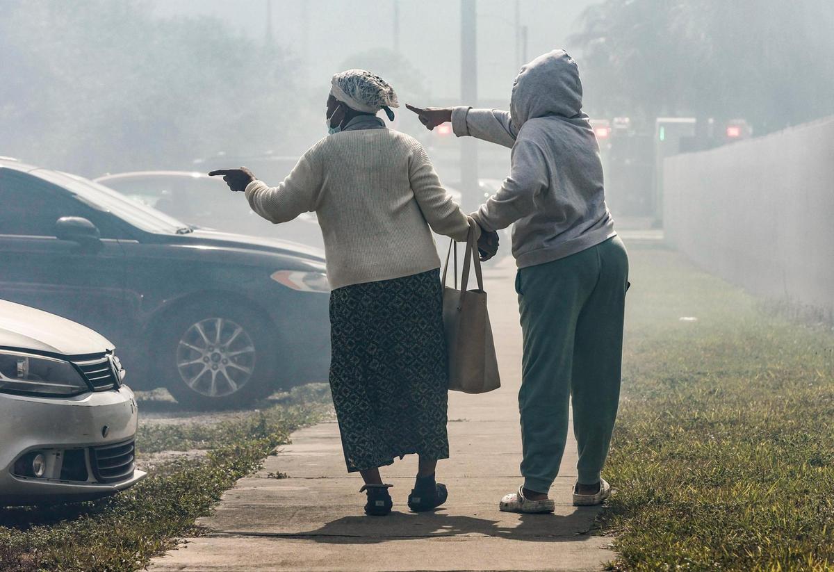 Francilia Jean, left, is assisted as she points toward a fire that engulfs her two-story apartment building at 395 NW 177th St. on Saturday morning, Jan. 28, 2023.