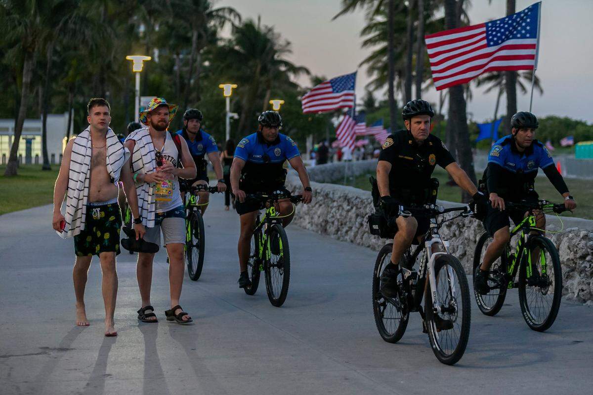 Beachgoers make their way through Lummus Park as police officers patrol nearby in Miami Beach during the start of Memorial Day Weekend on Friday, May 28, 2021.