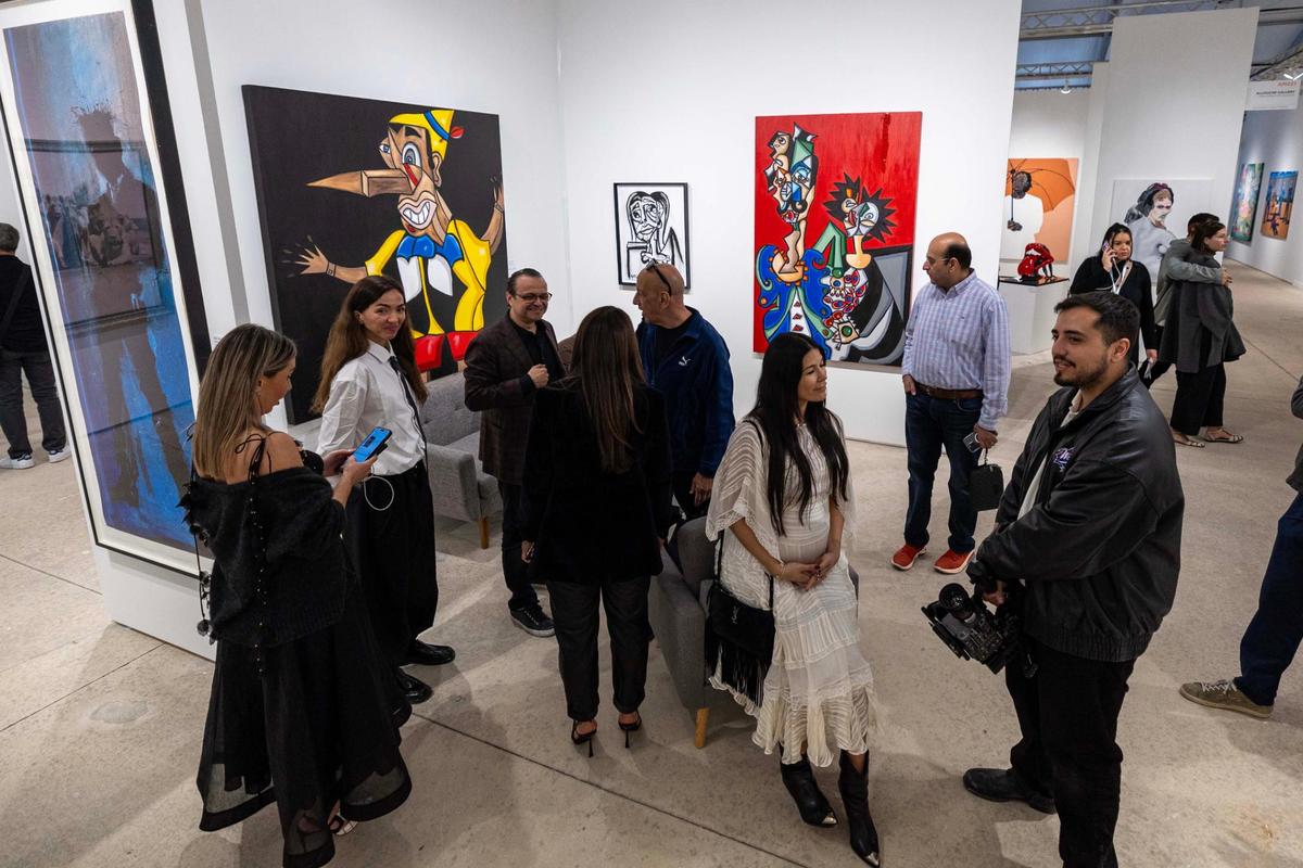 Guests socialize in front of paintings created by Andres Valencia, 13, being displayed during Art Miami at One Herald Plaza on Tuesday, Dec. 3, 2024, in Miami, Fla.
