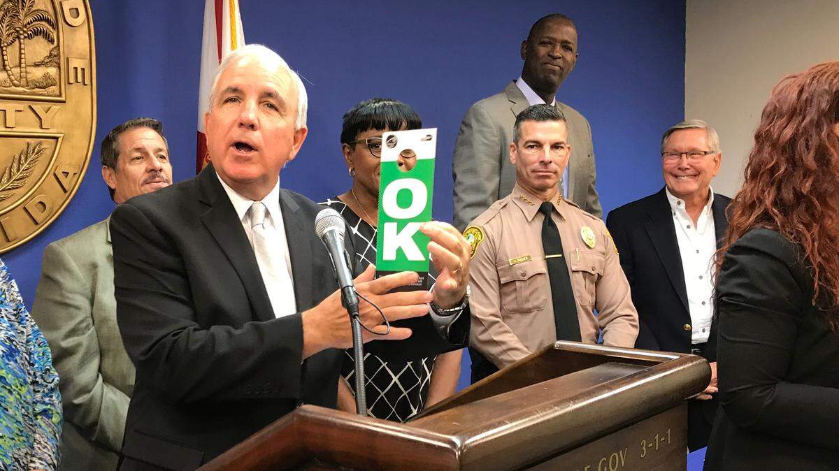 Miami-Dade Mayor Carlos Gimenez displays the “OK” side of new door hangers the county is mailing to more than 1 million households for use after a hurricane. The other side of the placard states “HELP,” and is designed to alert rescuers that someone inside needs assistance. The county says drones can pick up the rescue requests as well. Gimenez shared the door hangers at a May 29, 2019, press conference on the June 1 start of the Atlantic hurricane season. The press conferene was held at the county’s emergency-operations center in Doral.