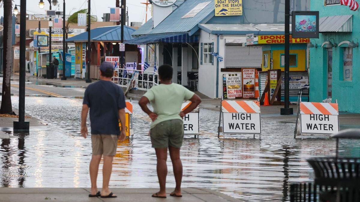 Todd Oerchen left, and Hazel Wood-MacArthur contemplates a flooded Dodecanese Blvd at the Tarpon Springs Sponge Docks on Monday, Aug 5, 2024, as tropical storm Debby continues its northbound track in the Gulf of Mexico.