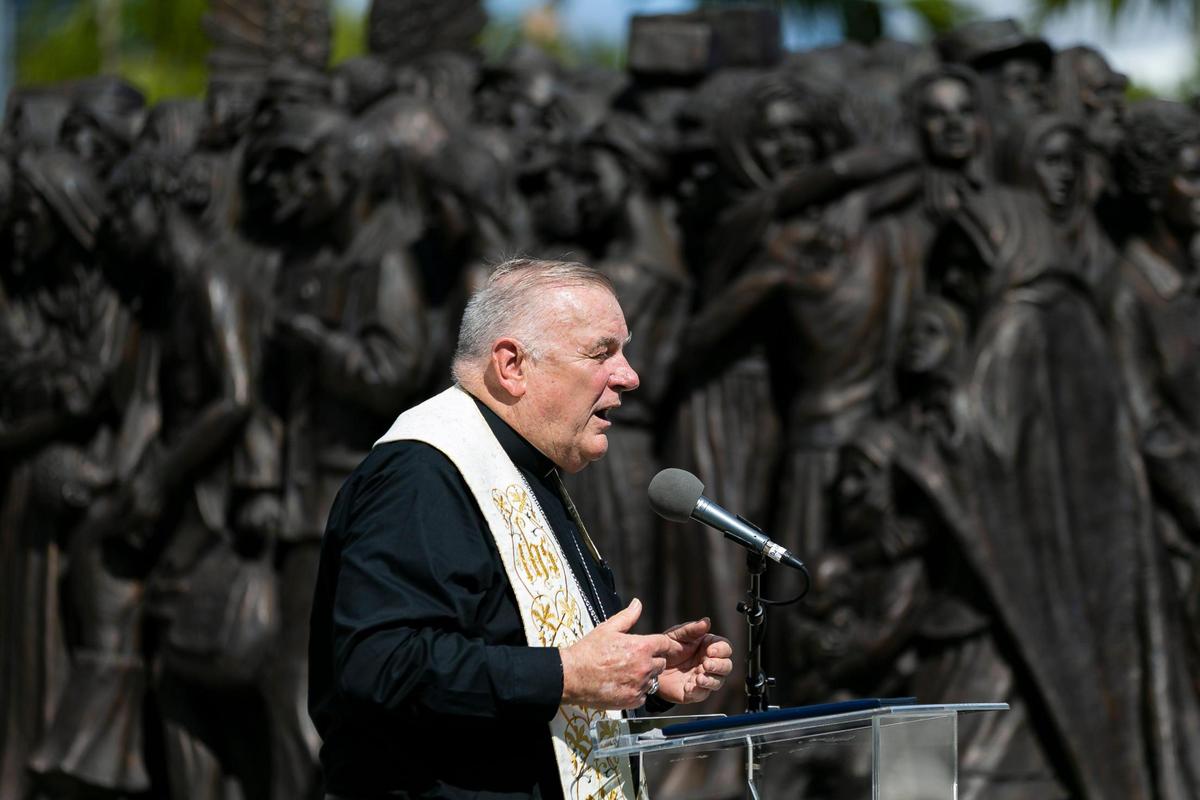 Archbishop Thomas Wenski speaks next to a sculpture titled “Angels Unawares,” at Bayfront Park in downtown Miami on Wednesday, February 10, 2021. The traveling bronze, life-sized sculpture will be open to the public daily for viewing until April 8. The sculpture weighs four tons and is 20-feet long. It features indigenous people, Jews fleeing Nazi Germany, Joseph, Mary, Jesus, and much more.
