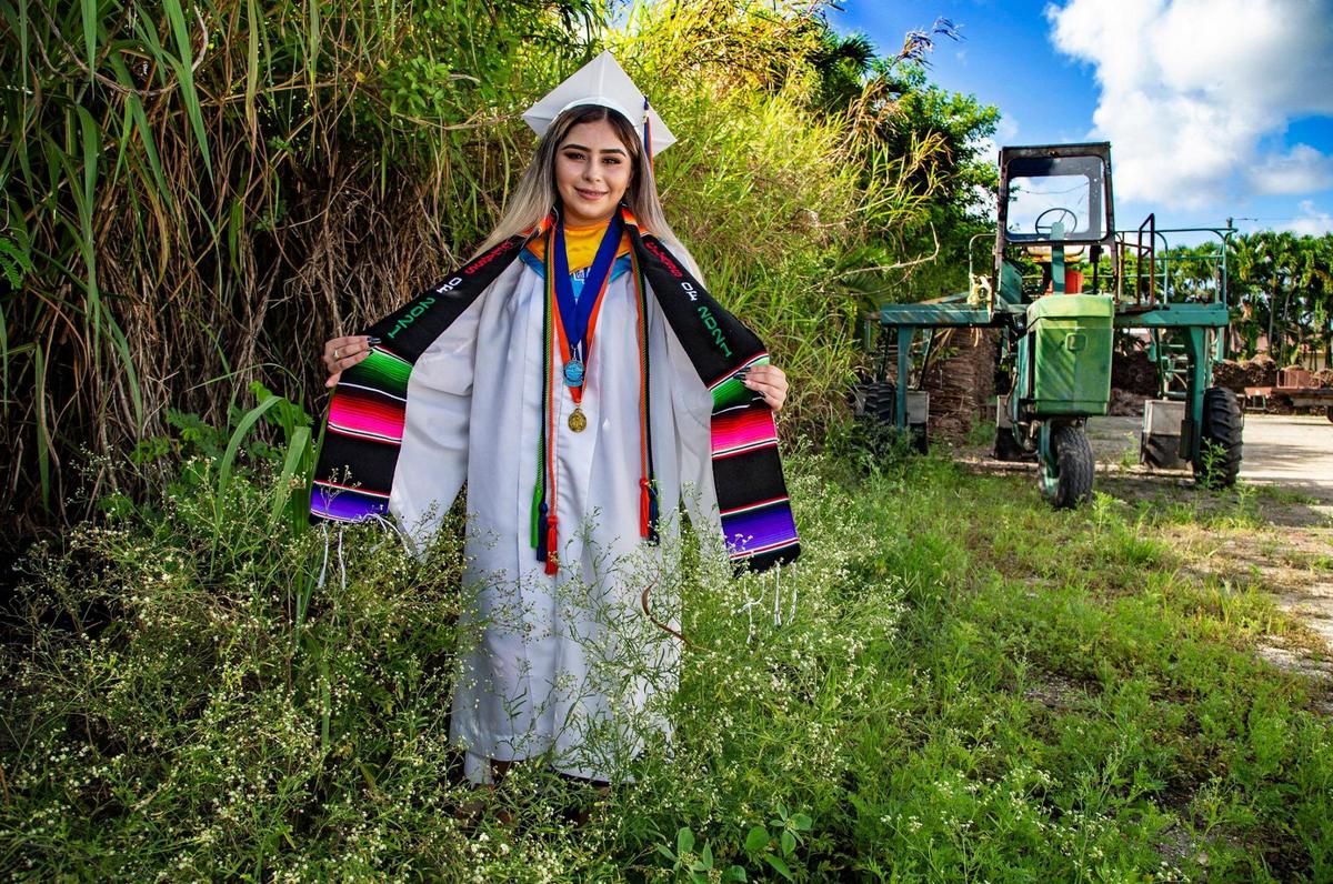 Elena Contreras, a graduate of Homestead Senior High School, wears her graduation cap and gown outside La Familia Produce & Repack LLC where she and her parents work on Wednesday, June 9, 2021.
