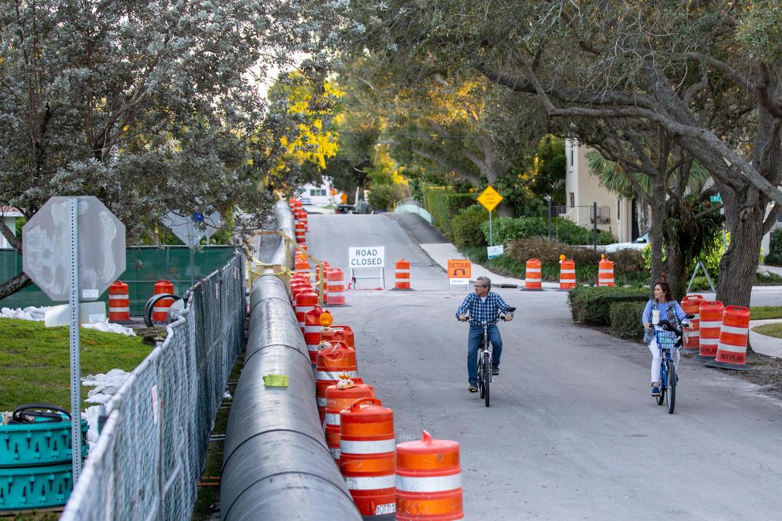 A couple rides their bikes past the temporary above-ground sewage pipe erected to temporarily resolve the sewage leak in the Rio Vista neighborhood in Fort Lauderdale on Tuesday, January 7, 2020.