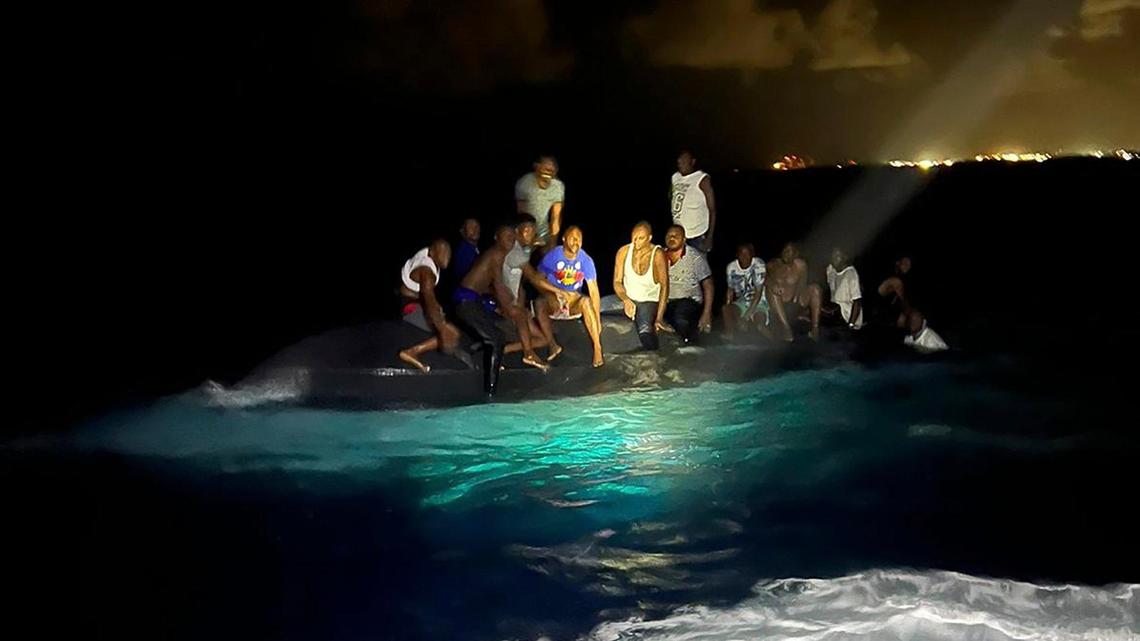 In this photo provided by the Royal Bahamas Defense Force, survivors sit on a capsized boat as they are about to be rescued near New Providence in the Bahamas, early Sunday, July 24, 2022. Bahamas Prime Minister Philip Brave Davis said in a statement that the dead included 15 women, one man and an infant. (Royal Bahamas Defense Force via AP)