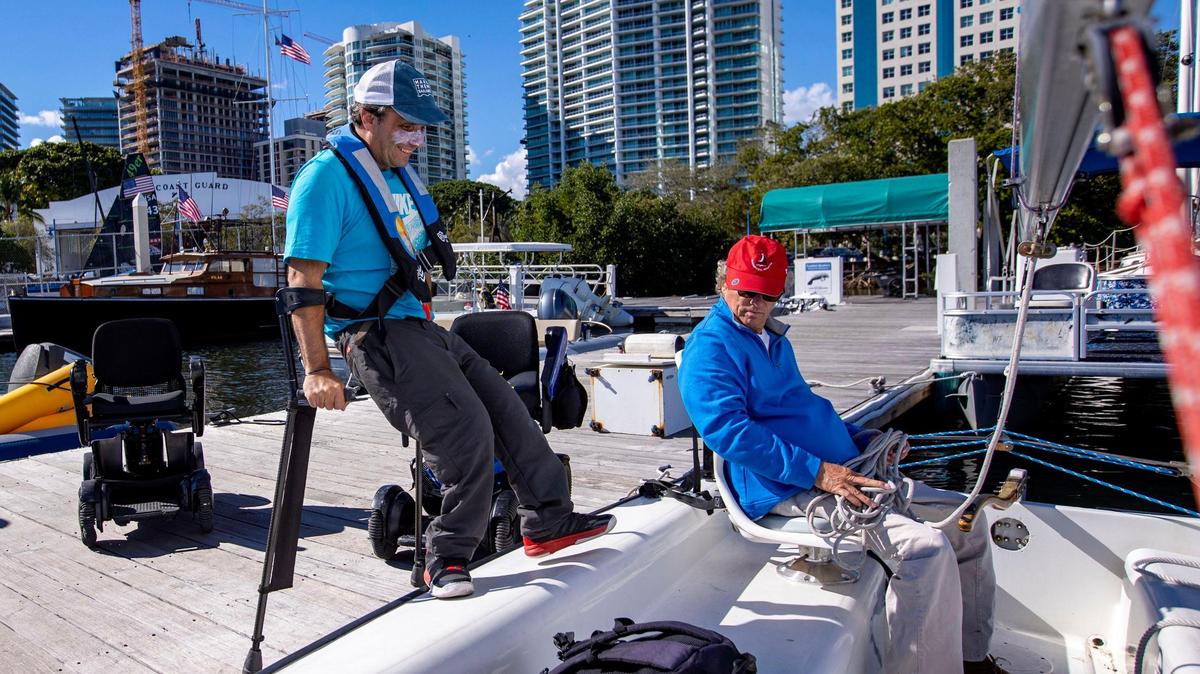 El navegante argentino Matías Paillot, de 44 años, sube a un velero mientras el fundador de Shake-A-Leg Miami, Harry Horgan, lo observa antes de navegar por la bahía de Biscayne, en Miami, el 12 de enero de 2023. La pareja navegó en un velero Freedom Independence diseñado para hacer la navegación accesible a personas con limitaciones físicas.