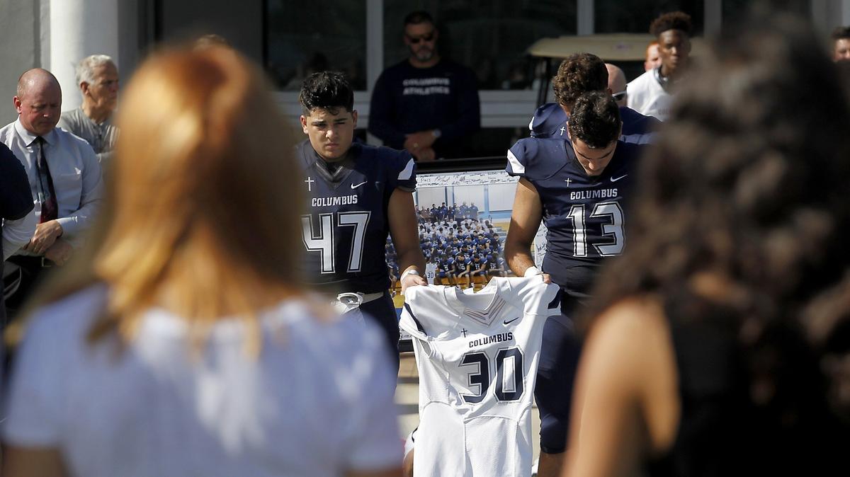 Columbus High School football players Patrick Silva, left, and Jorge de la Pedraja hold a football jersey with No. 30
to be presented to the parents of Ari Arteaga during a pregame ceremony honoring Ari, who died in a car crash on July 28. The ceremony remembering the son of UM assistant baseball coach J.D. Arteaga was held at Columbus High on Thursday, Aug. 23, 2018, before its football season opener against Mater Academy.