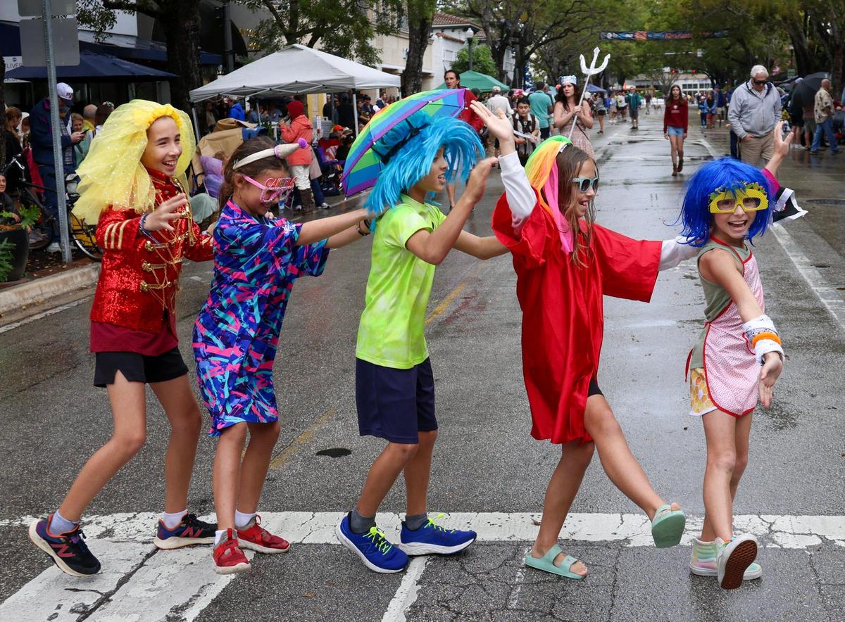 Dalia Roe, 11, left, Daphine Roe, 8, Liam Kelly, 11, Fiona Roe, 9, and Ayden Kelly, 9, form a conga line while dancing across the street prior to the start of the parade. It was singing, dancing, and parading in the rain as Coconut Grove held its annual satirical parade on Sunday, January 7, 2023 in Miami, Florida.
