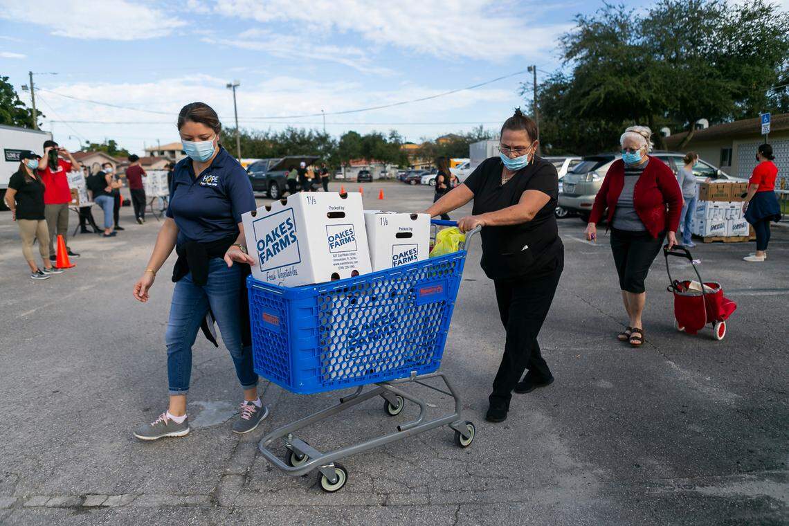 Fanny Montes, a community service specialist at Hope Mission Center, left, helps Yamila Gracia, center, and Encarnacion Carballo push their cart as they received free produce during a drive-thru food distribution event in Hialeah, Florida, on Saturday, December 5, 2020.
