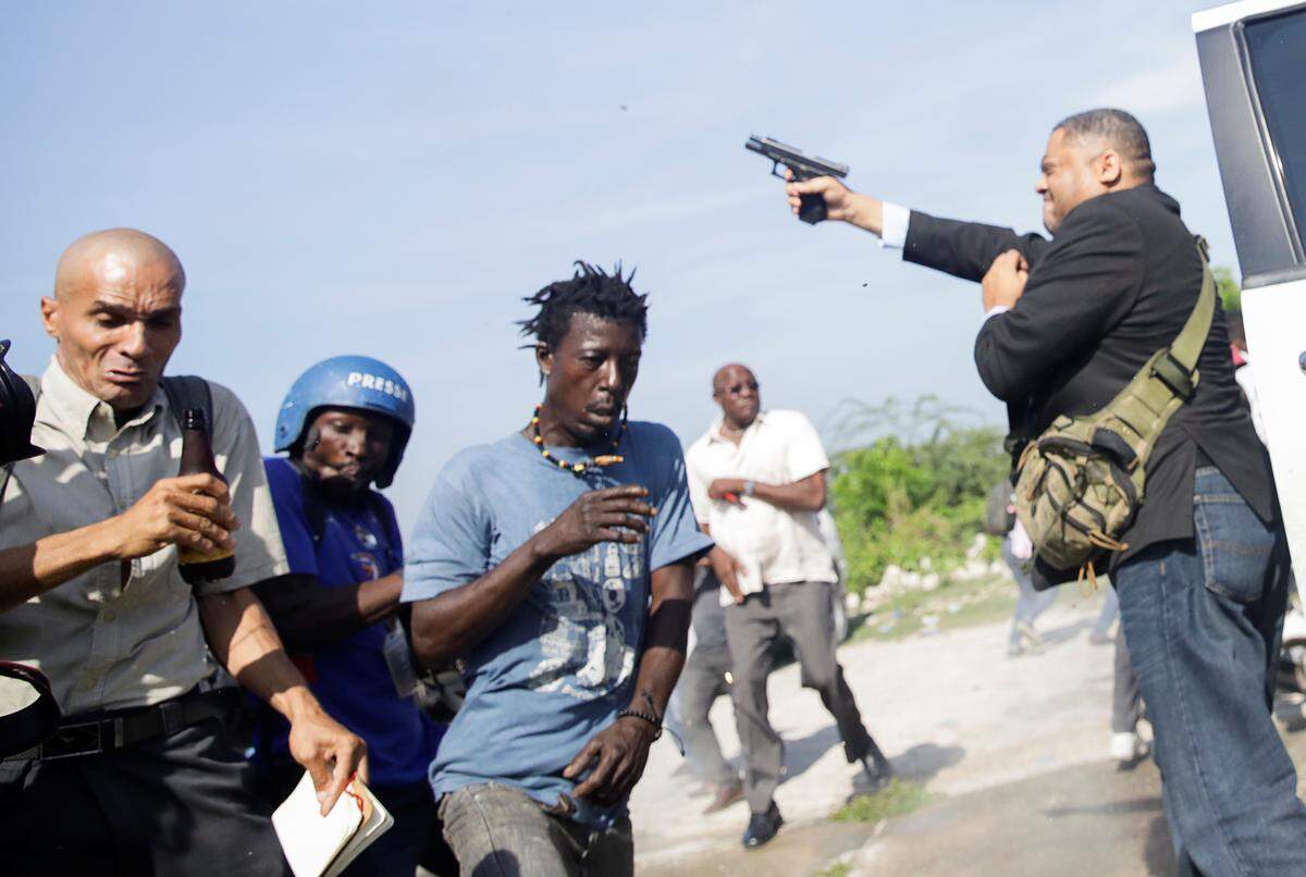 People run as Haitian Sen. Jean Marie Ralph Féthière fires a gun in Port-au-Prince on Sept. 23, 2019, in the yard of the Haitian Senate. Two individuals, an Associated Press photographer and a security agent for the Parliament, were shot and injured.