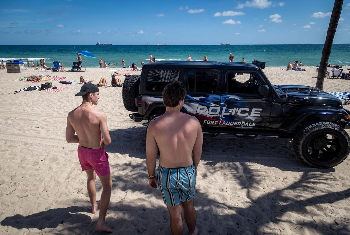 Two spring breakers from Michigan give a Fort Lauderdale police vehicle the right of way on the sands of Fort Lauderdale Beach on Feb. 28, 2024.