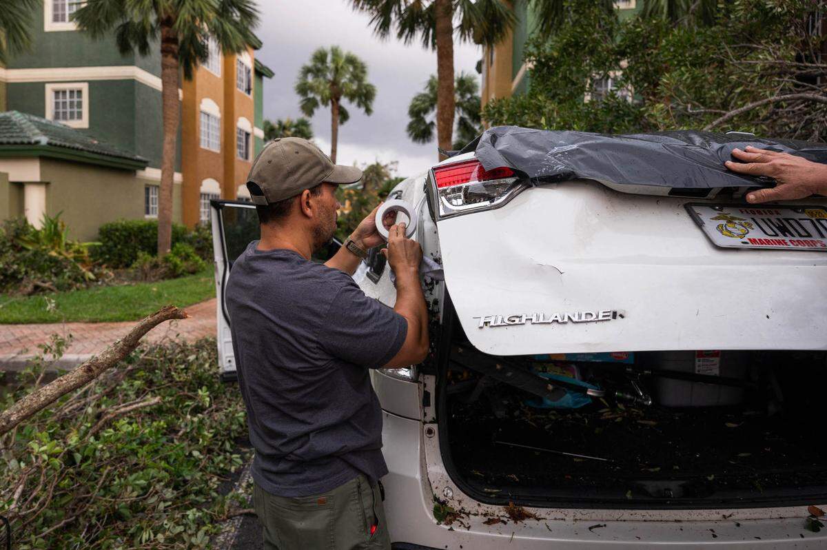 Samuel Tavarez, a resident at the Sanctuary Cove Apartment complex, attempts to cover the shattered windows of his car with tape and plastic tarp in the aftermath of a Saturday evening tornado on Sunday, April 30, 2023, in Palm Beach Gardens, Fla. The National Weather Service confirmed an EF-1 tornado touched down in Palm Beach Gardens Saturday evening.