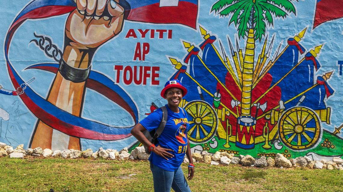 Edwina Larson wears a hat and a shirt with the Haitian flag motive in Little Haiti ahead of the Haiti’s Flag day celebration, on May 18th, in Miami, on Saturday May 17 2025. The mural is an SOS for Hait and reads “Haiti is Suffocating.”